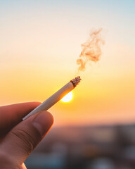 Hand holding burning cigarette with smoke at sunset