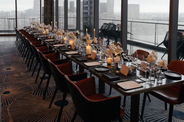  Panoramic view of a refined black table setting with white roses, handmade plates, natural wood chairs, and glasses. Elegant decor with fresh flowers for a sophisticated event atmosphere.