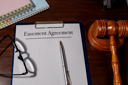 A legal easement agreement rests beside a judge&rsquo;s gavel on a wooden desk, symbolizing land rights, property access, and legal boundary arrangements.