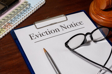 An eviction notice document lies beside a gavel on a wooden desk, representing legal proceedings,...
