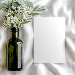 a minimalist wedding card mockup on table with white table cloth, 5x7 wedding program mockup standing up, lemon leaf greenery, sage greenery, eucalyptus greenery and tiny white flowers, cozy feel