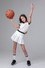 Beautiful teenage girl with long hair in a white sports skirt and top with a basketball in a photo studio on a white background. Sportswoman. Basketball. Youth.