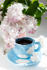 a cup with clouds on a blue background with tea. A strong hot drink for breakfast, a bouquet of lilacs in a vase