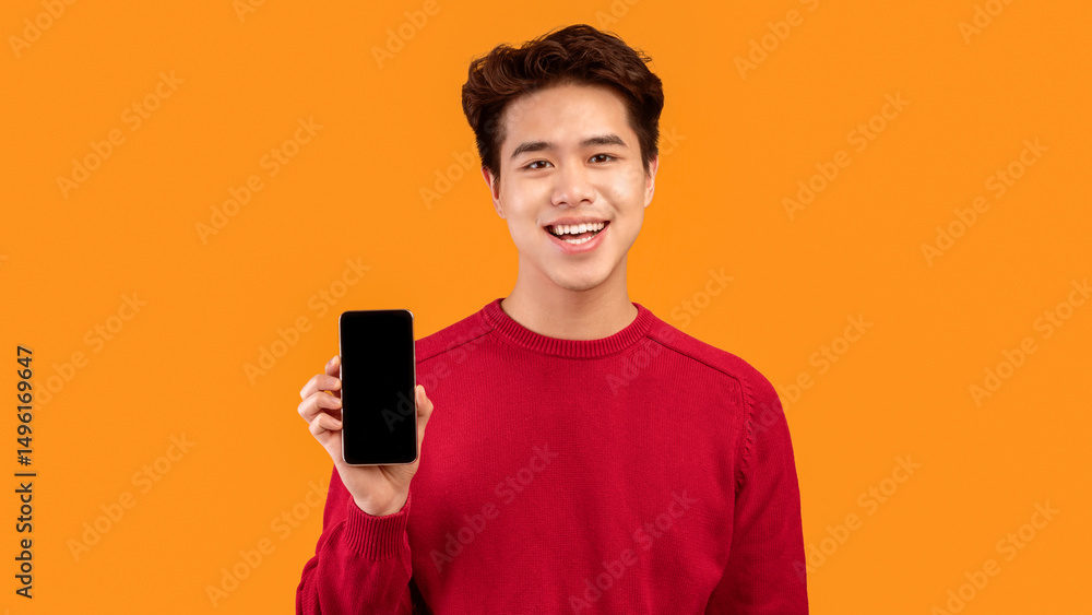 Poster I Recommend This App. Smiling asian guy holding smartphone with black empty screen in hand and showing it to camera. Gadget with blank space for mock up, isolated over orange studio background