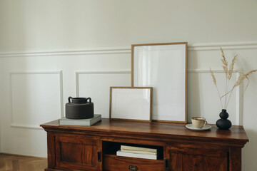 Scandinavian interior design. Modern living room. Set of blank picture mock up poster frames. Mahogany wooden dresser sideboard. Black vases with dry grass. Cup of tea, coffee. White wall background.