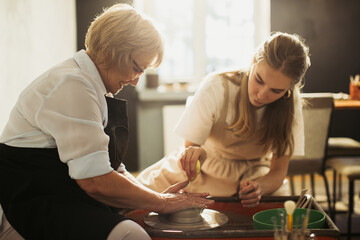 Senior woman learning pottery with young instructor using pottery wheel