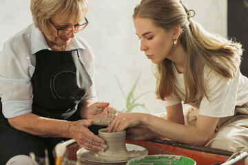 Senior potter teaching apprentice clay modeling on pottery wheel
