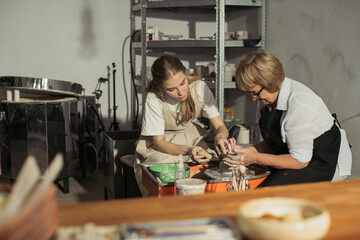 Senior woman learning pottery making with young instructor