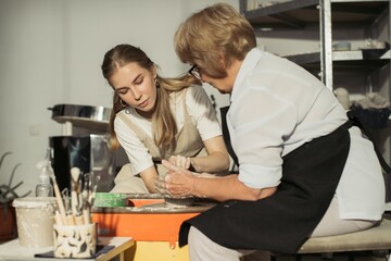 Obraz premium Senior potter teaching apprentice clay modeling on pottery wheel