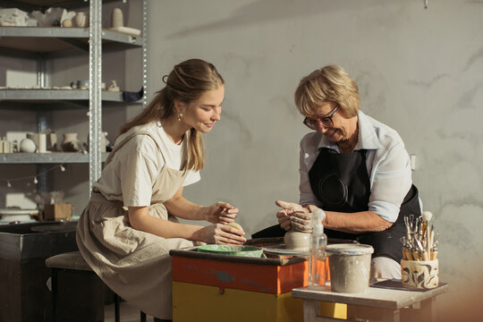Senior woman learning pottery with young apprentice in workshop