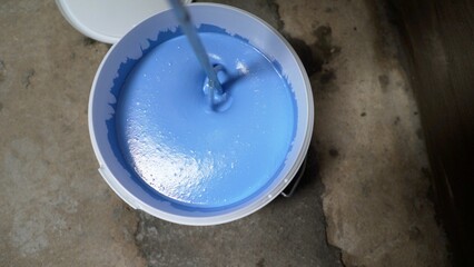 Mixing blue paint in bucket with mixing paddle on construction site