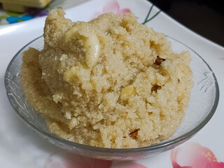 Close-up of homemade suji halwa served in a glass bowl. This rich Indian semolina dessert is garnished with ghee-roasted nuts and flavored with cardamom.