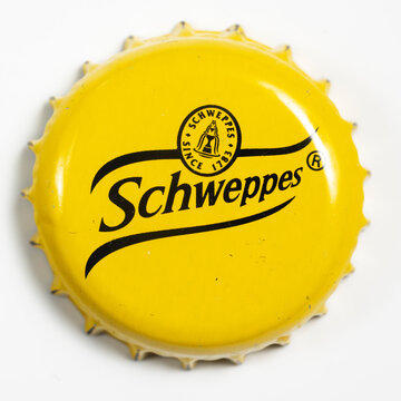 A close-up of a bright yellow Schweppes bottle cap with the black Schweppes script logo and a small circular emblem with "SCHWEPPES" and "SINCE 1783"