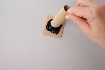 Drop black paint onto a flat surface. Dip the toilet paper roll into the paint.
