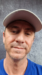Close-up of man with baseball hat in light gray color. The man has forty years and light eyes and...