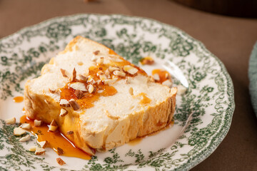 A close-up captures a slice of traditional caramelized egg white pudding known as molotof or molotov, generously drizzled with golden syrup and sprinkled with almond pieces, on a decorative plate