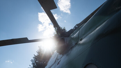 A Soviet-era helicopter stands against a clear sky, its rotor blades illuminated by the sun's rays,...