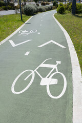 Obraz premium Marked bike lane with white bicycle symbols and arrows on a green paved path surrounded by grass and vegetation, promoting urban cycling and safe transportation in Portugal
