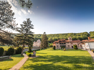 Wide garden view of Celije Monastery near Valjevo, Serbia: stone church and monastic residence sit by, lawns and forested hills. Manastir Celije is a serbian orthodox monastery.