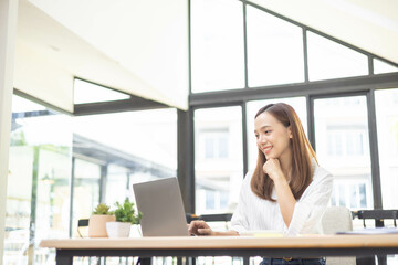 Obraz premium A woman is working at a desk in an office with a laptop, a mobile phone and a pile of documents. She is smiling and happy. 