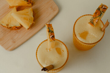 Two glasses of pineapple juice with cinnamon sticks and pineapple wedges