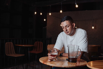 young latin man with long hair holding a glass of beer in a bar while looking at the camera