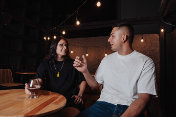 young latin man with long hair holding a glass of beer in a bar while looking at the camera