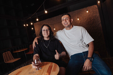 young latin man with long hair holding a glass of beer in a bar while looking at the camera
