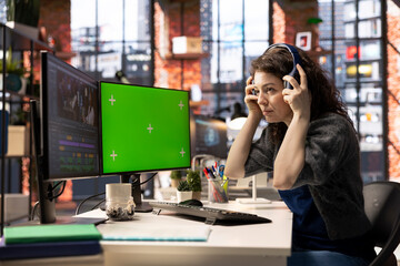 Female videographer making a movie montage next to green screen display, multitasking with a dual...