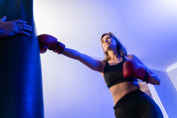 Female boxer training with personal coach using punch mitts in blue-lit gym