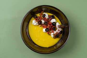 A mouthwatering creation rests in a dark bowl, featuring a creamy, vibrant yellow base topped with...