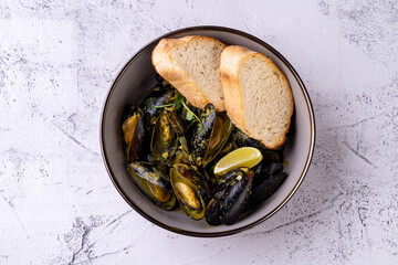 A vibrant bowl of fresh mussels cooked in aromatic herbs and spices, accompanied by slices of crusty bread, invites a culinary adventure. The presentation exudes comfort and warmth