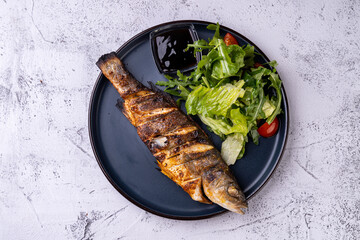 A beautifully plated grilled fish, seasoned to perfection, rests alongside vibrant greens and...