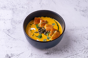 A delightful bowl of creamy pumpkin soup sits elegantly, topped with crispy croutons and a drizzle of herb oil, ready to be savored. A perfect reflection of autumn's warmth and flavors