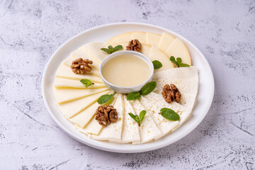 A beautifully arranged cheese platter showcases an array of gourmet cheeses accompanied by fresh mint and walnuts. The creamy dipping sauce adds an enticing touch to this culinary delight