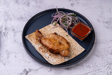 Juicy grilled chicken rests on a warm flatbread, accompanied by thinly sliced onions and a bowl of zesty sauce. This delightful dish invites exploration of rich flavors