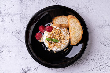 A beautifully arranged dish showcases creamy cheese adorned with toasted pine nuts and ripe raspberries, accompanied by crispy bread slices