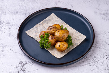 Savory roasted golden potatoes are artfully arranged on a textured plate, accompanied by vibrant greens. This dish showcases a rustic charm while inviting a sensory experience of flavor and warmth