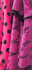 Close-up of vibrant pink fabric featuring black polka dots and floral lace with ruffled edges,...