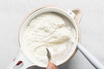 overhead view of All purpose flour in a sieve, top view of sifting baking flour into a large bowl