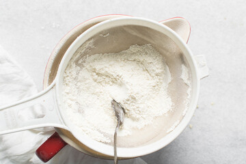 overhead view of All purpose flour in a sieve, top view of sifting baking flour into a large bowl