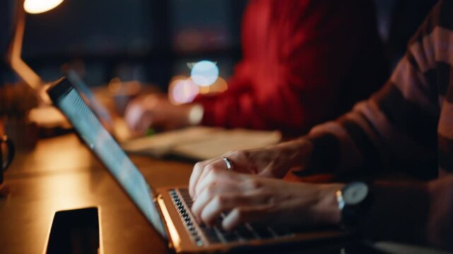 Hardworking professionals typing laptops at dark office closeup. Two colleagues