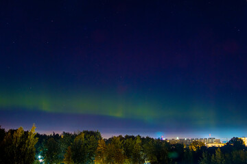 Northern lights over city. Pale light of Aurora borealis in night sky. Color flashes in northern hemisphere.