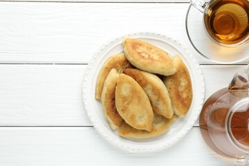 Delicious fried pyrizhky (stuffed pies) and tea on white wooden table, flat lay. Space for text