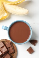 Tasty chocolate milk in cup, pieces and banana on white wooden table, flat lay