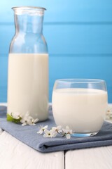 Fresh milk and blossoms on white wooden table against light blue background, closeup