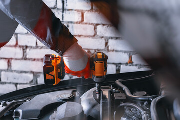 Close-up of a mechanic using a cordless drill while repairing a car engine. Concept of car...