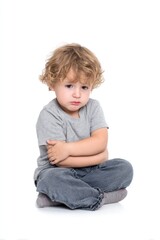 Sad young child sitting cross-legged with arms folded, looking down, on a white background.