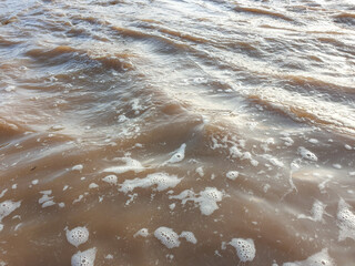 Brown Murky River Water Flowing Rapidly With Surface Ripples and Foam