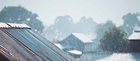Rain falls on metal rooftops in a rural area, with trees and houses visible in the background, creating a calm and refreshing atmosphere.